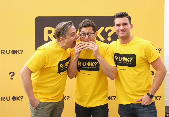 Three males pose in front of an R U OK day banner; they are wearing yellow t-shirts with the R U OK logo