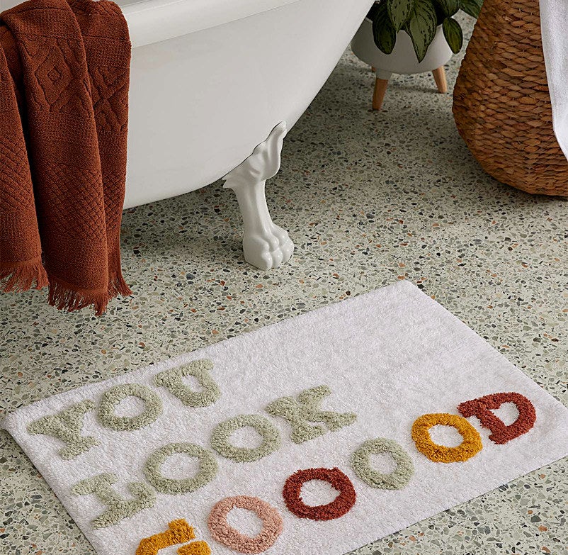 The bath mat that says &quot;you look gooood&quot; on the floor beside a bathtub