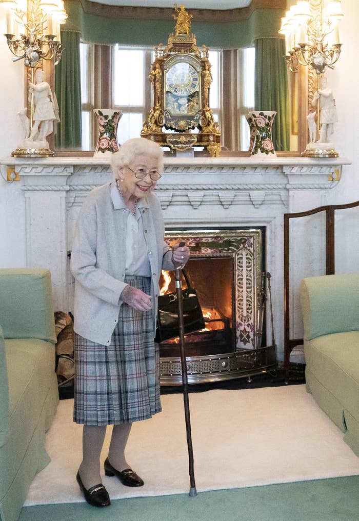 The Queen standing in front of a fireplace with a cane and smiling