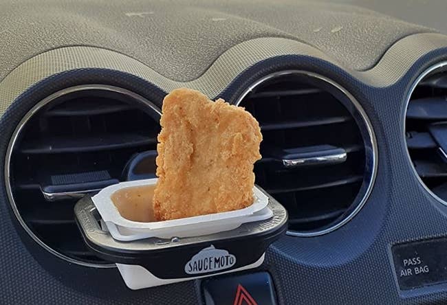 The dip clip clipped onto a reviewer's car air vent with sauce and a nugget in it