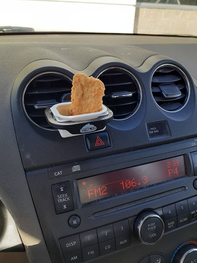 The dip clip clipped onto a reviewer's car air vent with sauce and a nugget in it