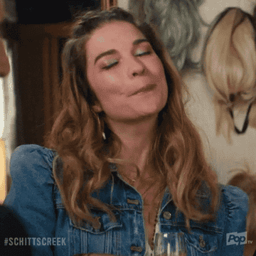 a gif of annie murphy from schitt&#x27;s creek smiling smugly