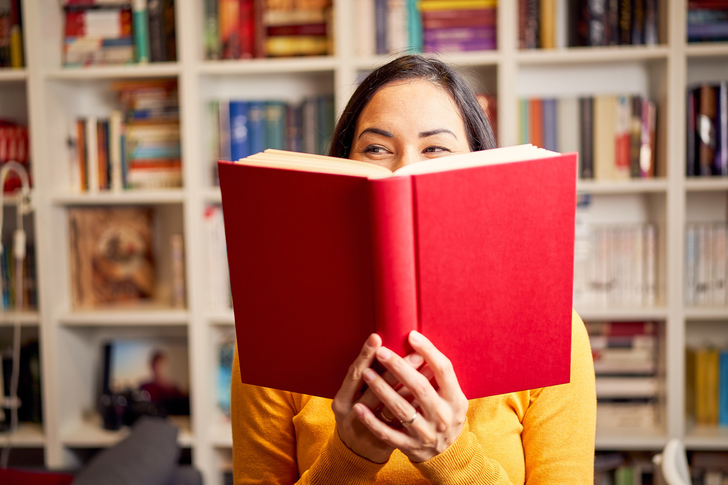a woman smiling behind a book