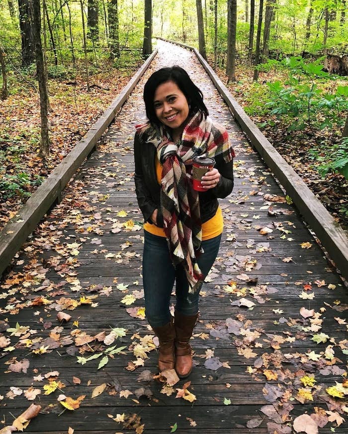 a reviewer photo of a person wearing the plaid scarf on a leaf-strewn walkway