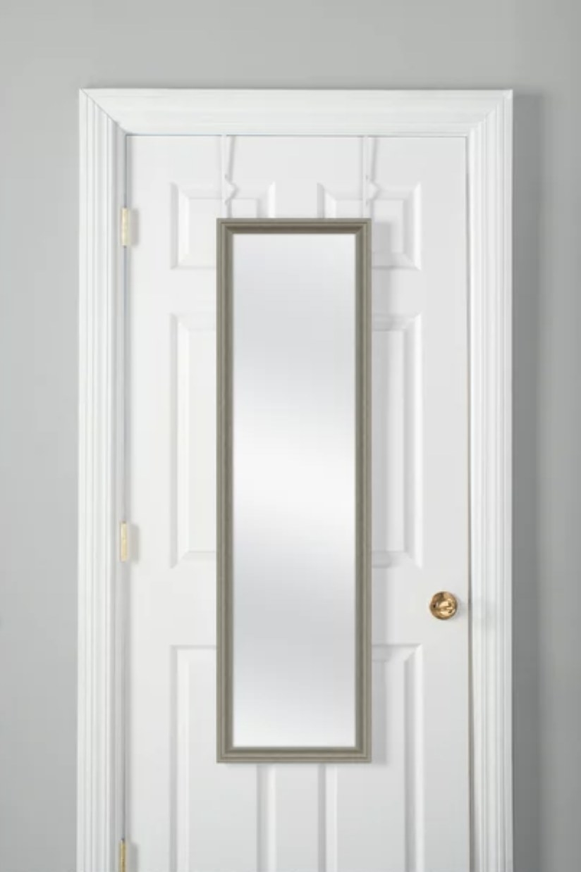 The rustic mirror hangs on the white door