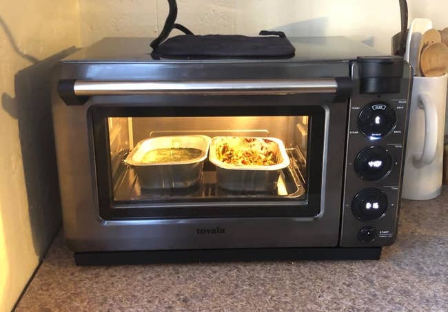 The smart oven in the color dark grey that a reviewer is using to cook two pans of food