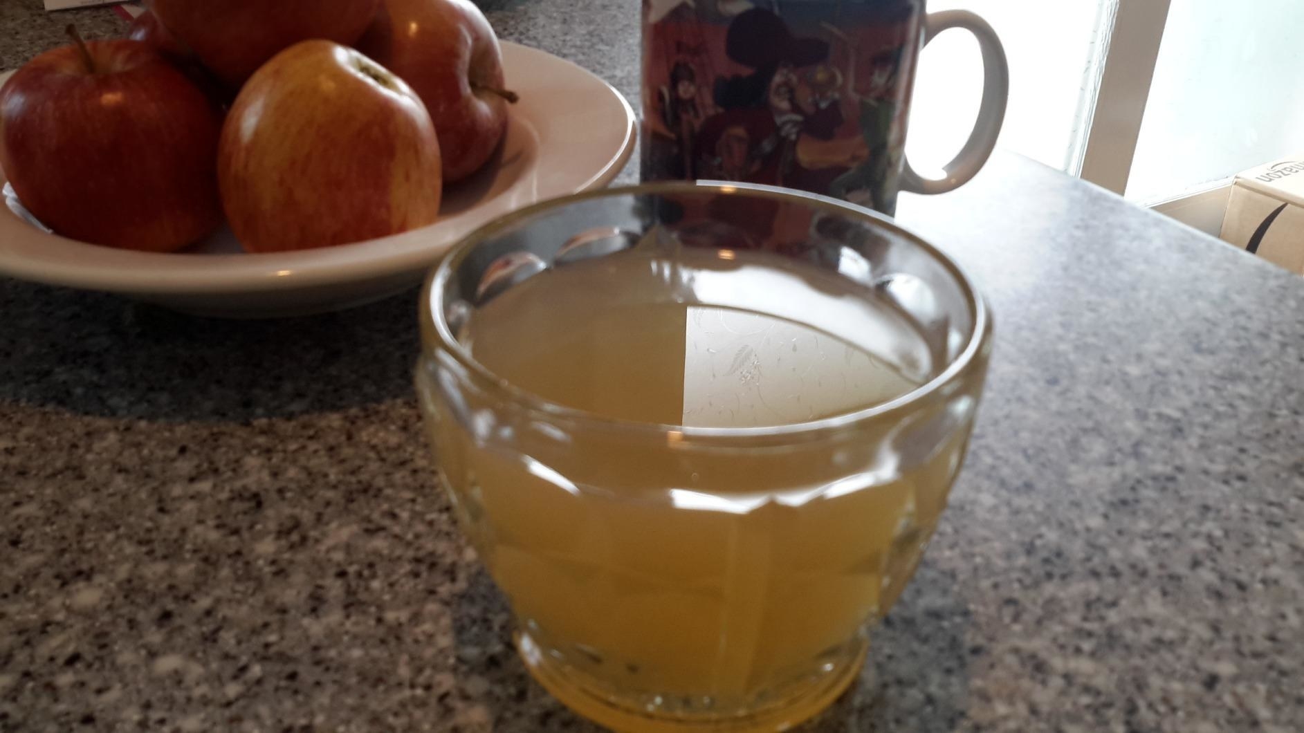 a reviewer photo of a cup of cider on a counter with a bowl of apples