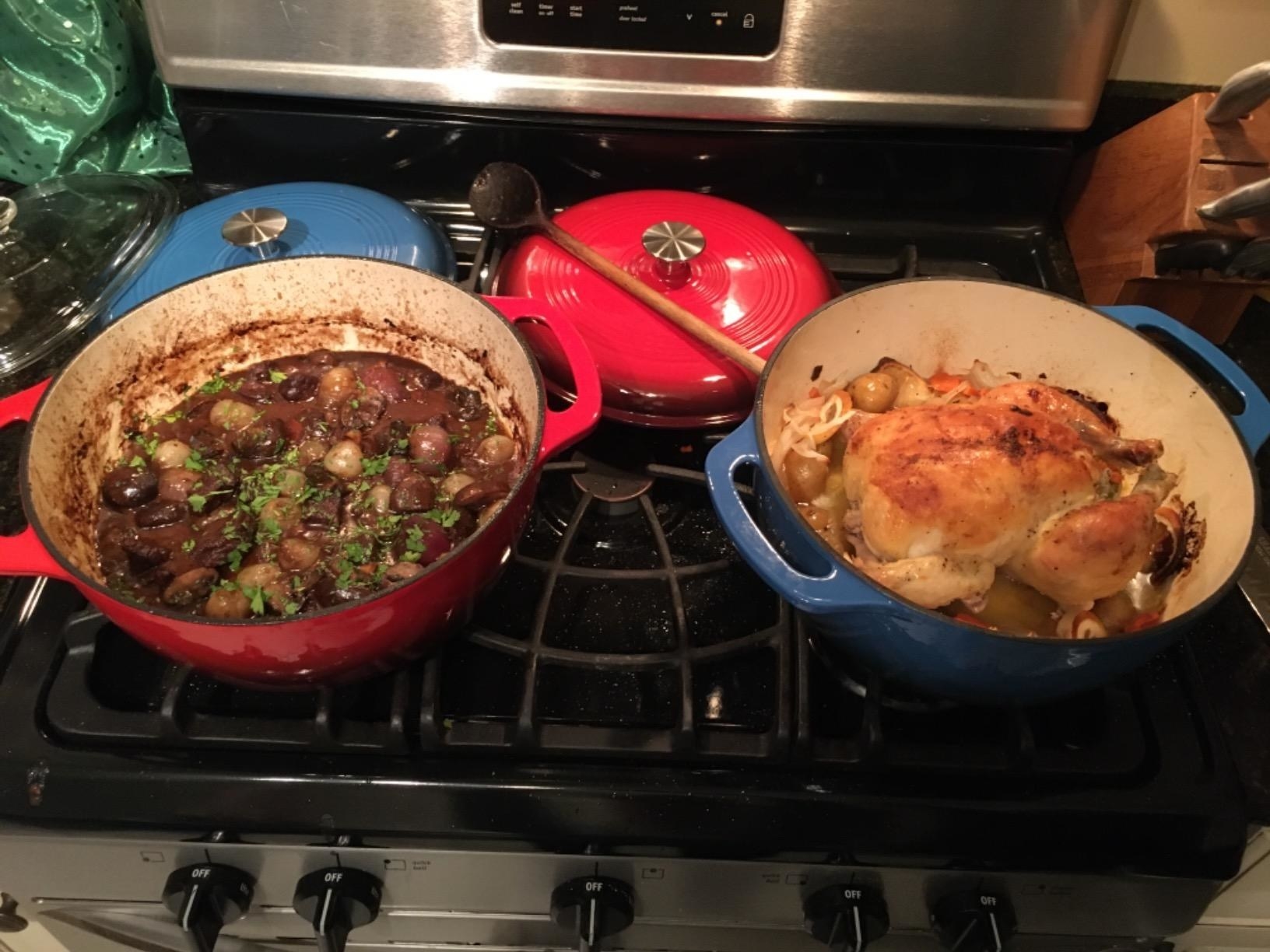 a reviewer photo of the red and blue Dutch ovens on a stove, one has mushrooms and one has a whole roasted chicken