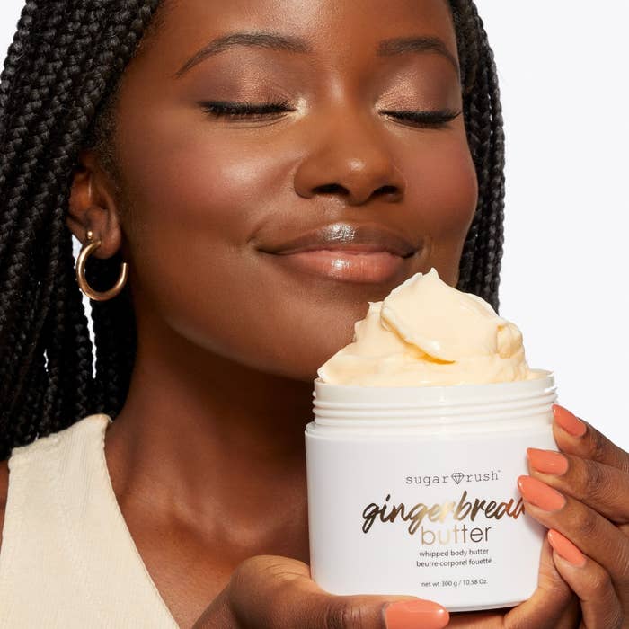 A person with braids holding a jar of body butter