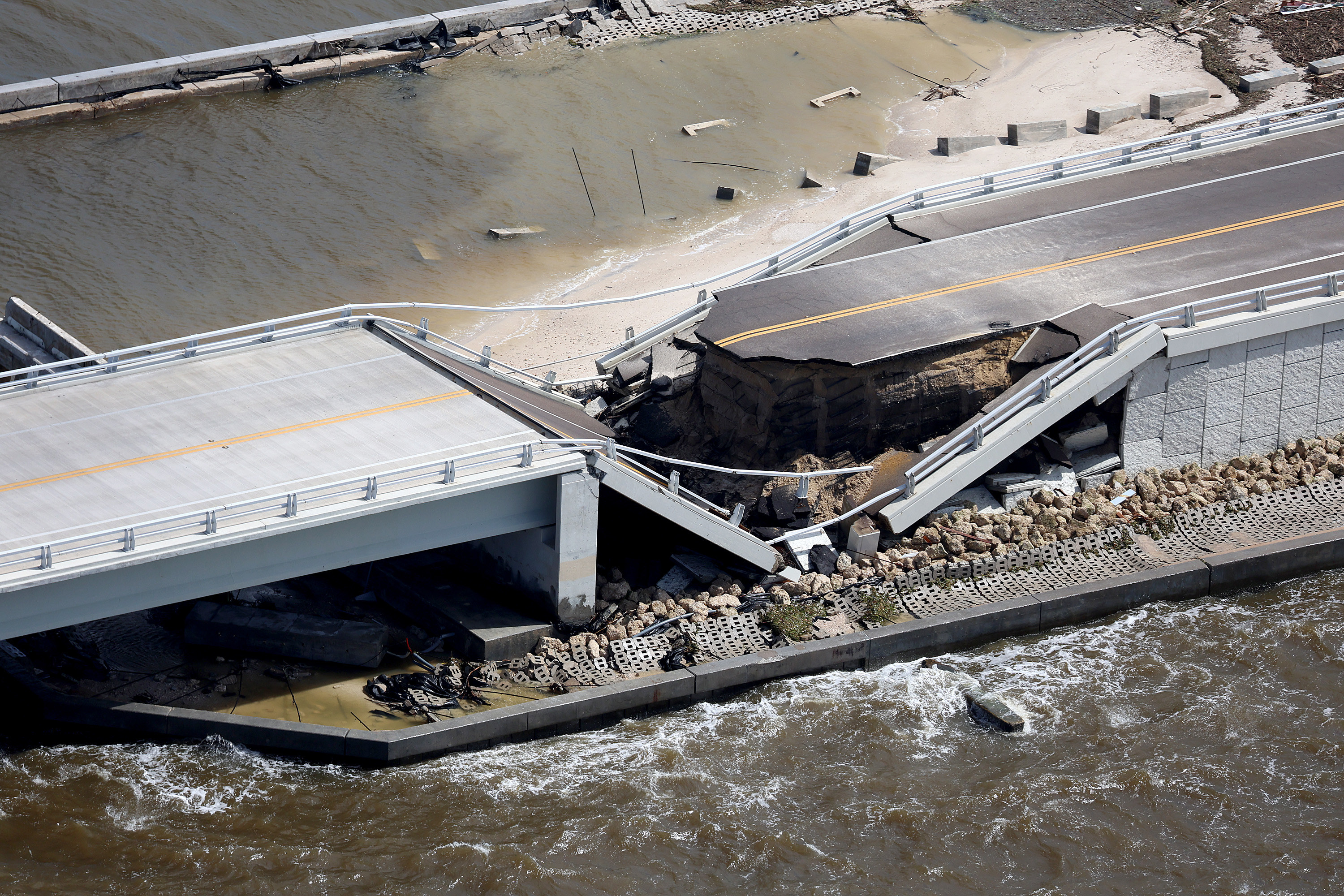 A bridge over a body of water is collapsed, with the two-lane road not connecting