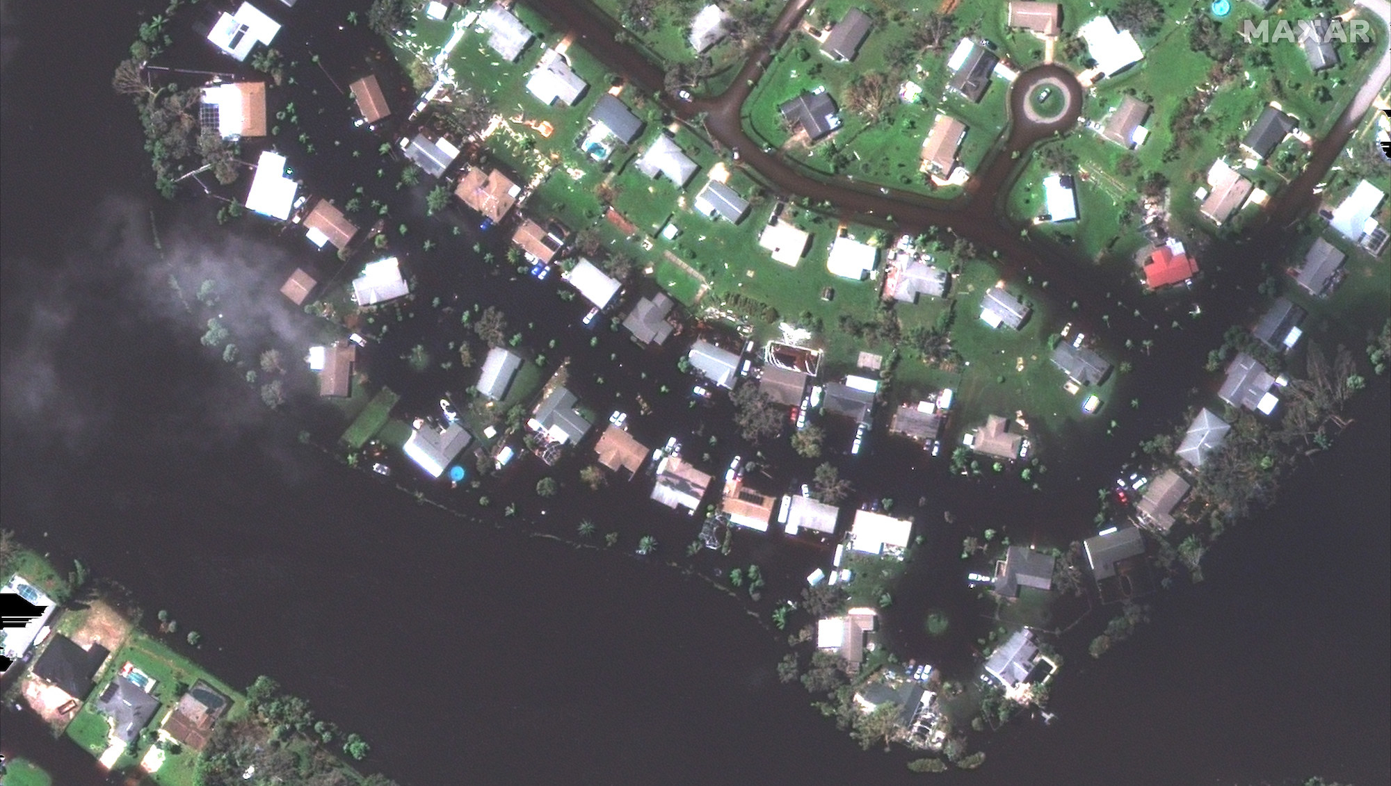 A satellite view shows a flooded neighborhood and rows of homes underwater