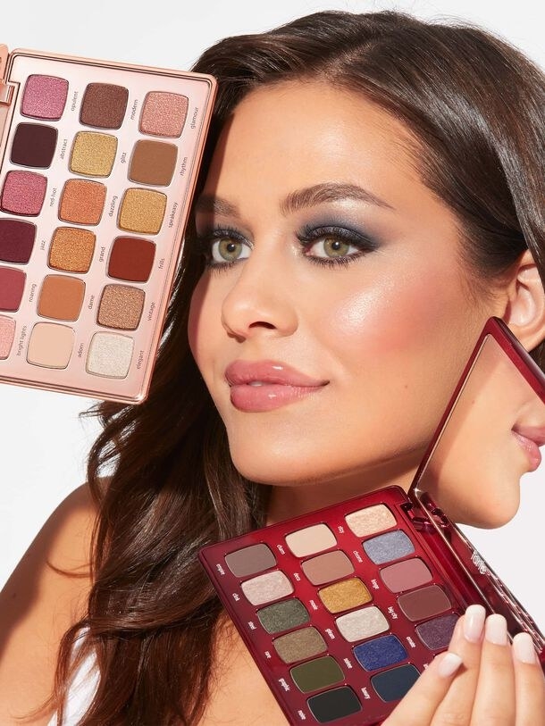 A person wearing makeup holding two eyeshadow palettes