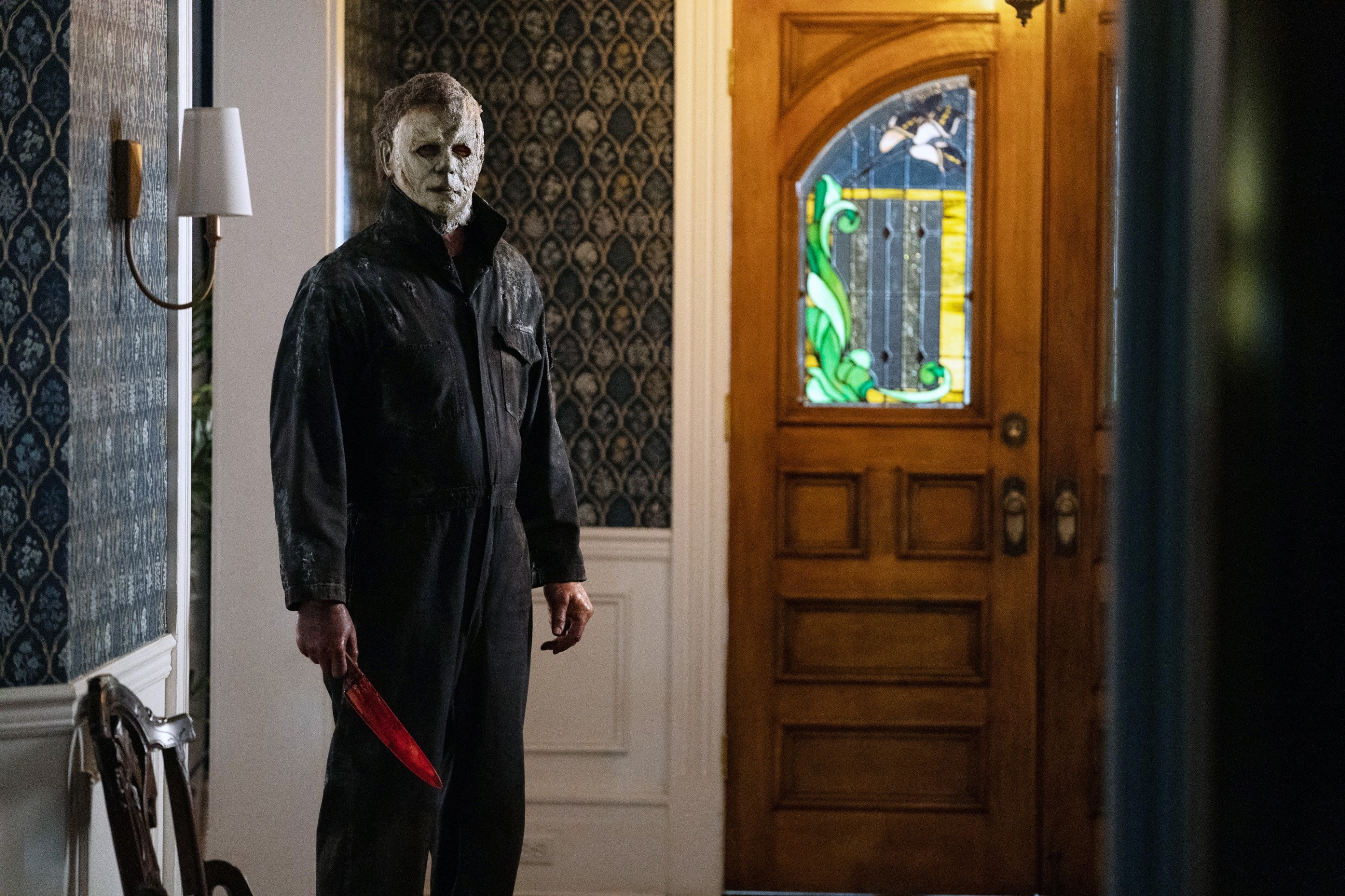 Michael Myers holding a knife and standing by a door in a hallway