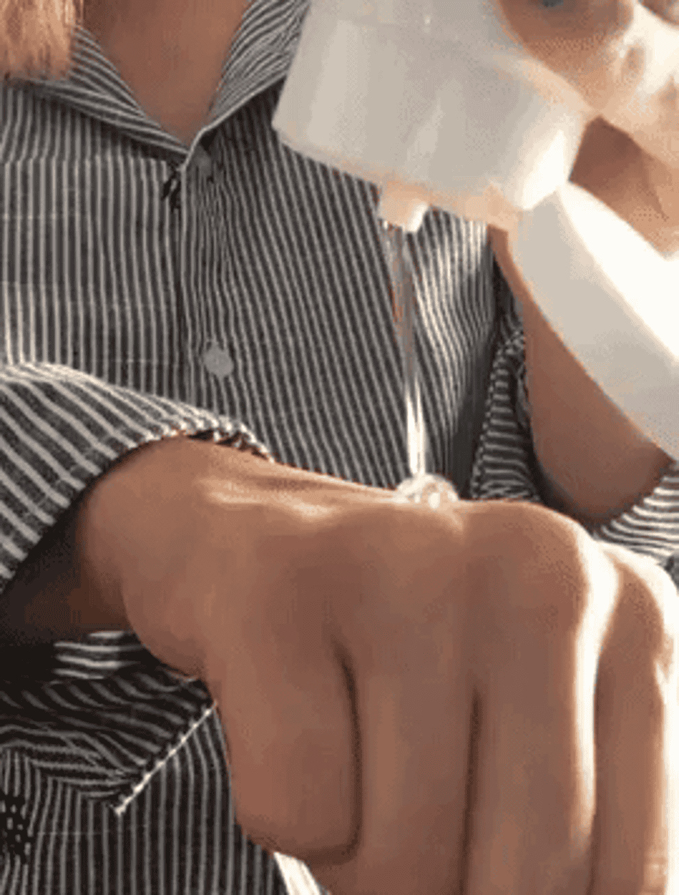 A person wearing a striped shirt squeezes a transparent gel onto the back of their right hand.