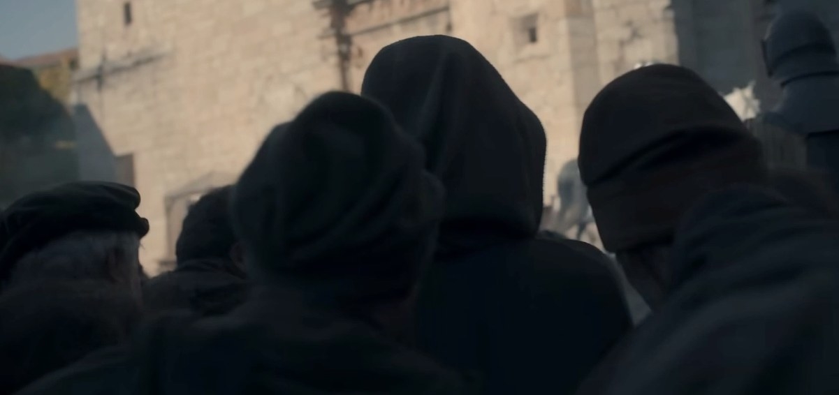 A hooded figure moves through a crowd in King&#x27;s Landing.