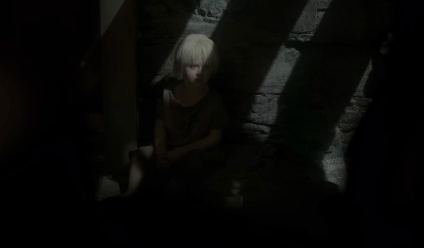 A small blonde child sits in shadows
