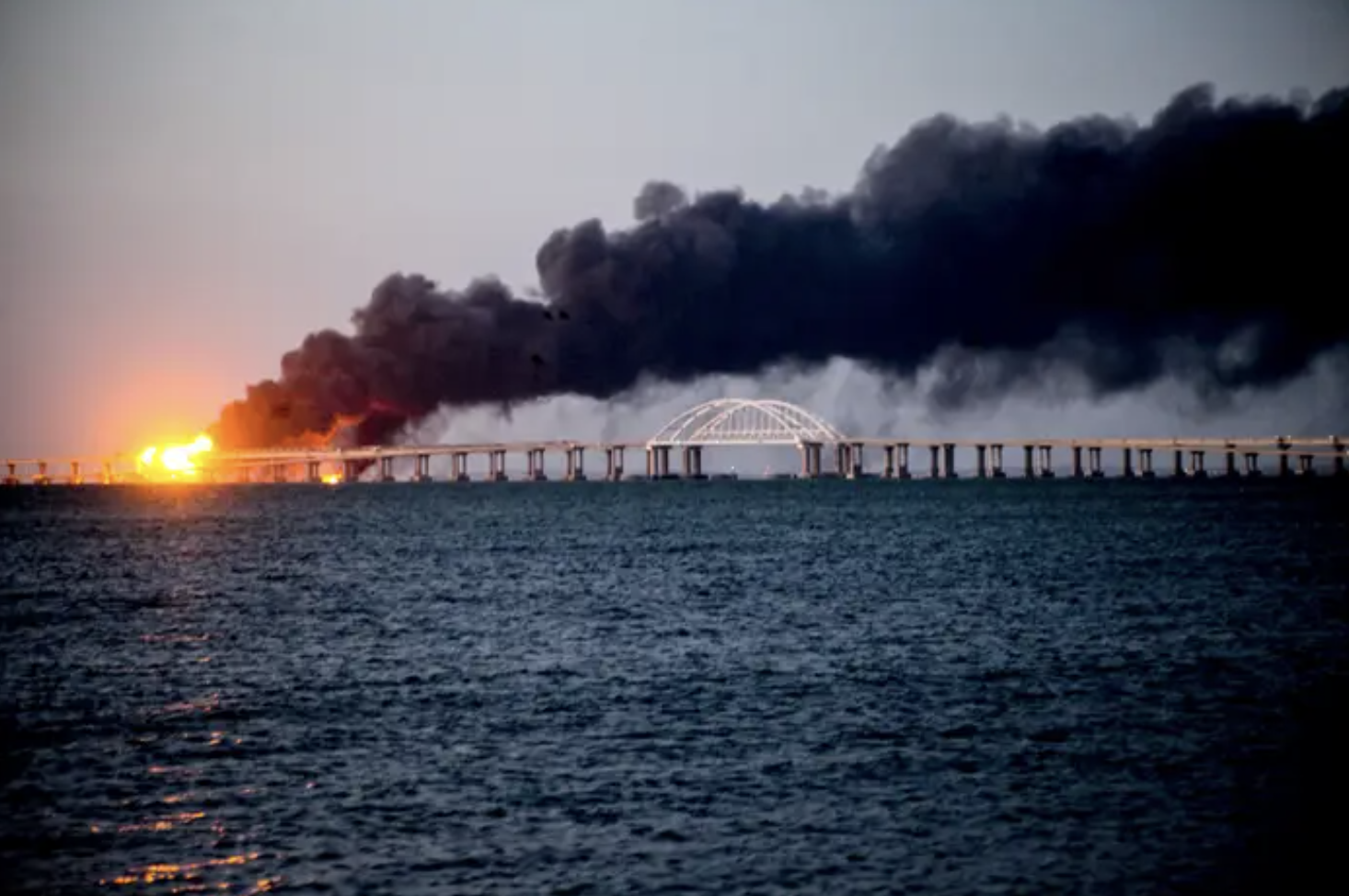 A bridge over water on fire and smoking