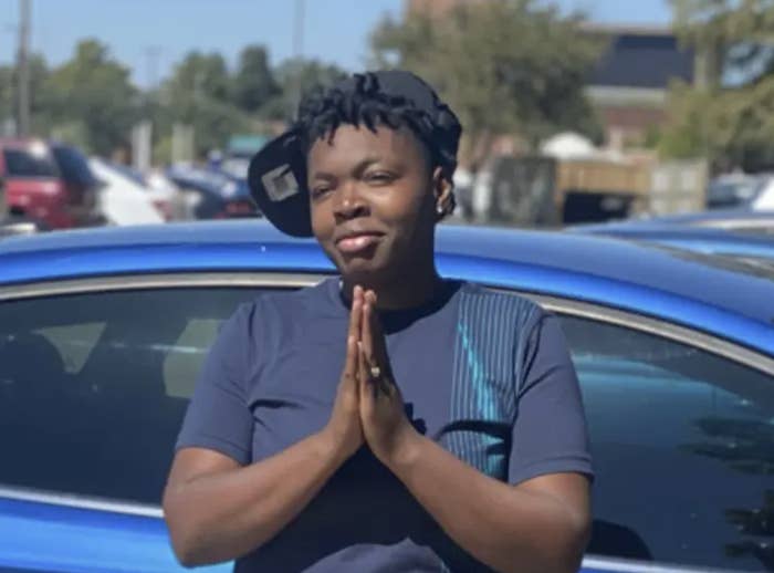 A photo of 21-year-old Asia Womack standing in front of a car with prayer hands