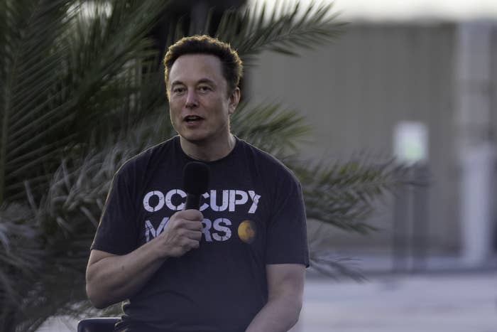Elon holding a mic and speaking as he wears a t-shirt that says &quot;Occupy Mars&quot;