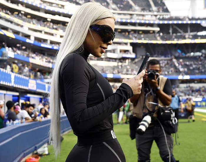 Kim holds her phone out to take a photo while standing on the field