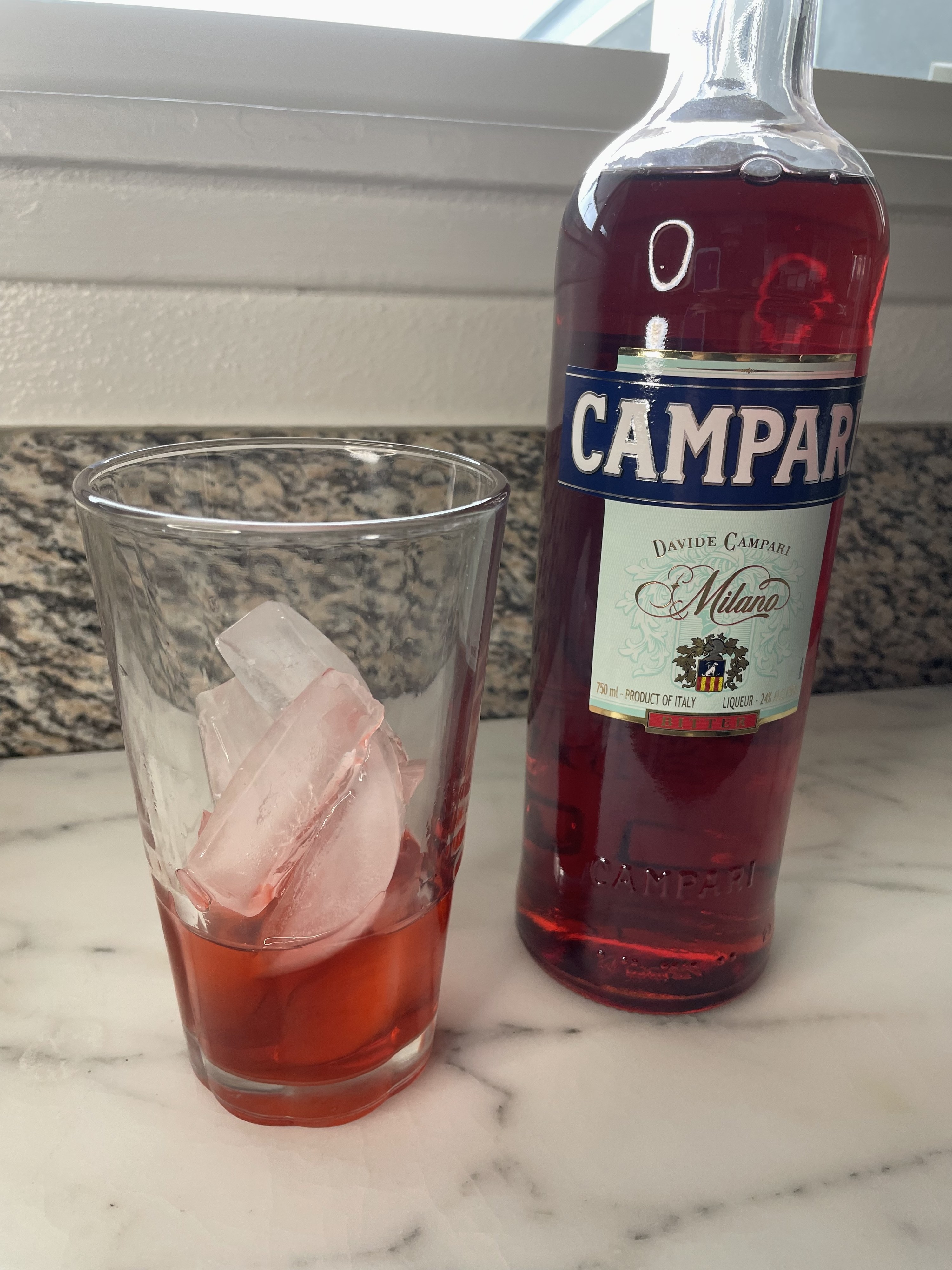 A cup of ice with Campari next to the bottle