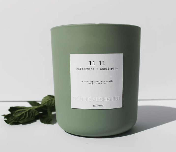 a candle in a sage green container with 11:11 on it