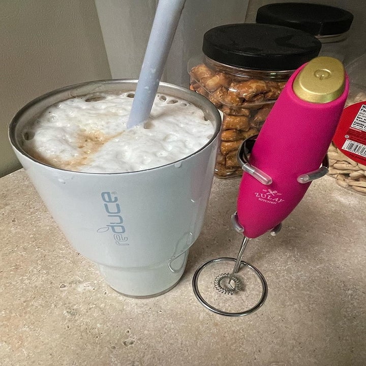 a pink frother next to a cup with frothy milk on the top