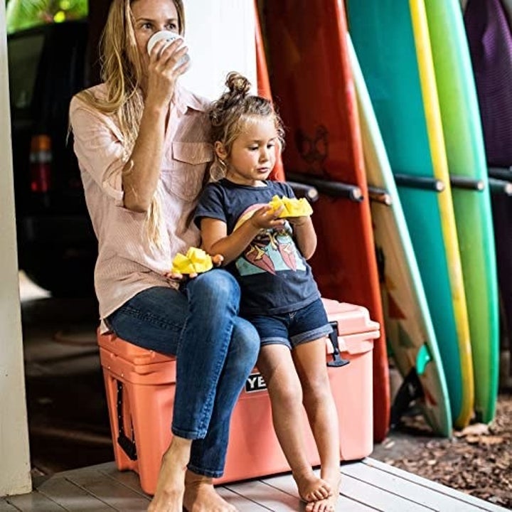 a woman and child sitting on a pink cooler