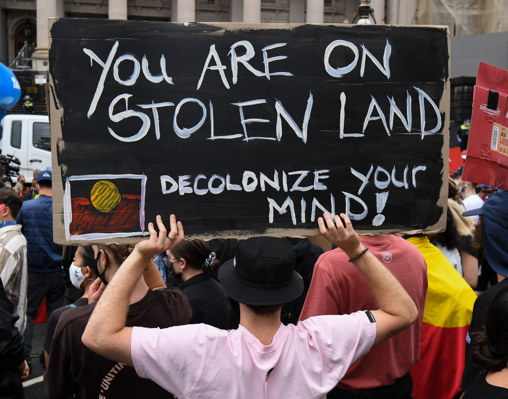 A man holding a sign at a protest in Australia saying &quot;You are on stolen land! Decolonise your mind&quot;