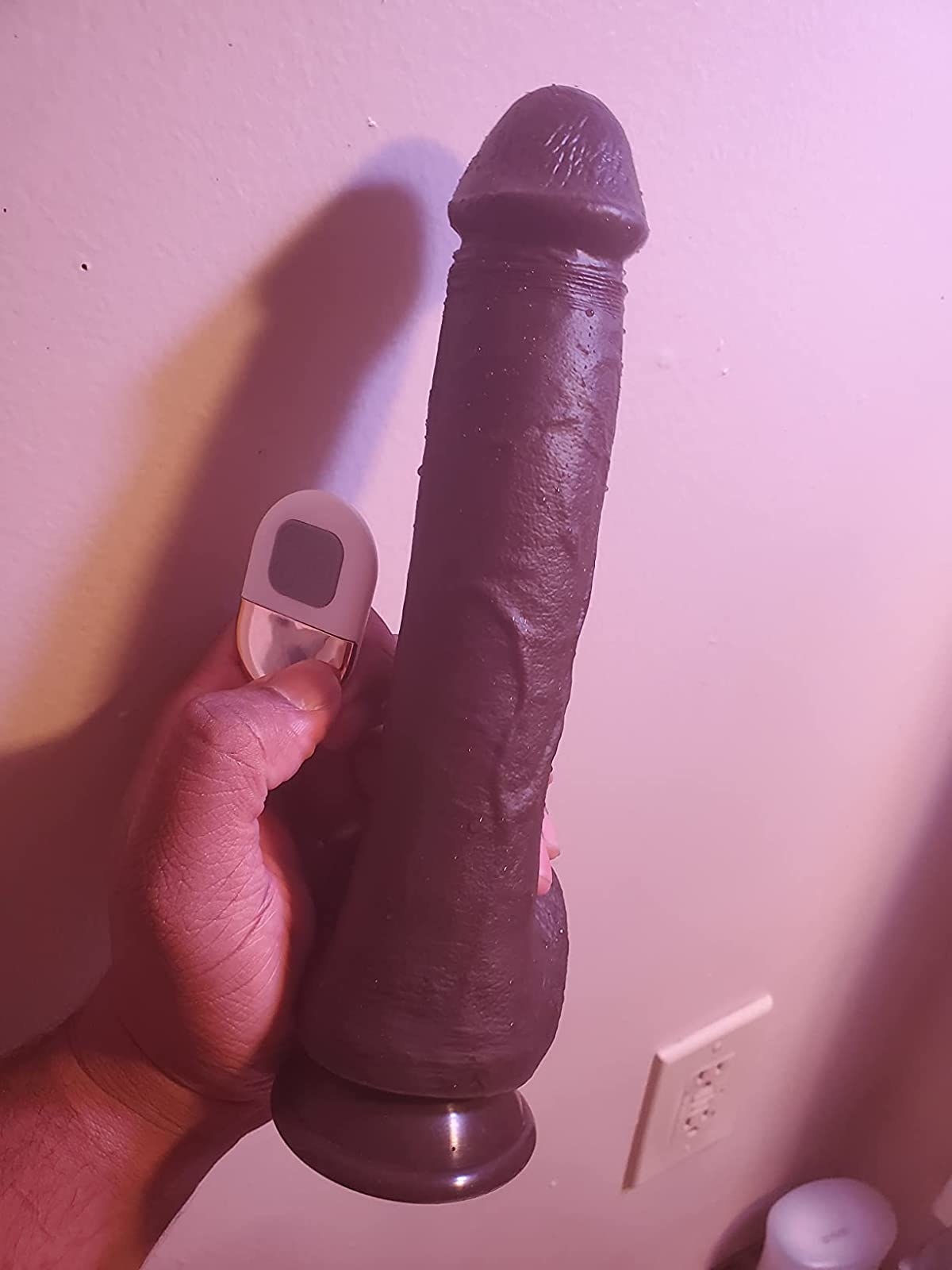 Reviewer holding brown thrusting dildo and white wireless remote