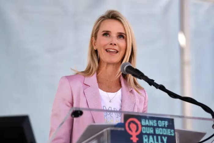 Jennifer Siebel Newsom wears a pink blazer and speaks at a podium