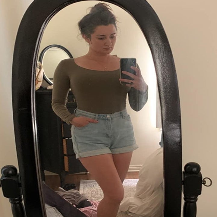 reviewer wearing the green bodysuit with denim shorts