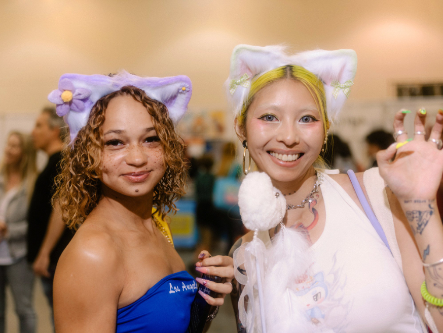 two people in fuzzy cat ears wave and smile at the camera
