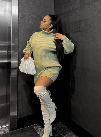 reviewer wearing balloon sleeve sweater dress in a light green shade with high heeled boots