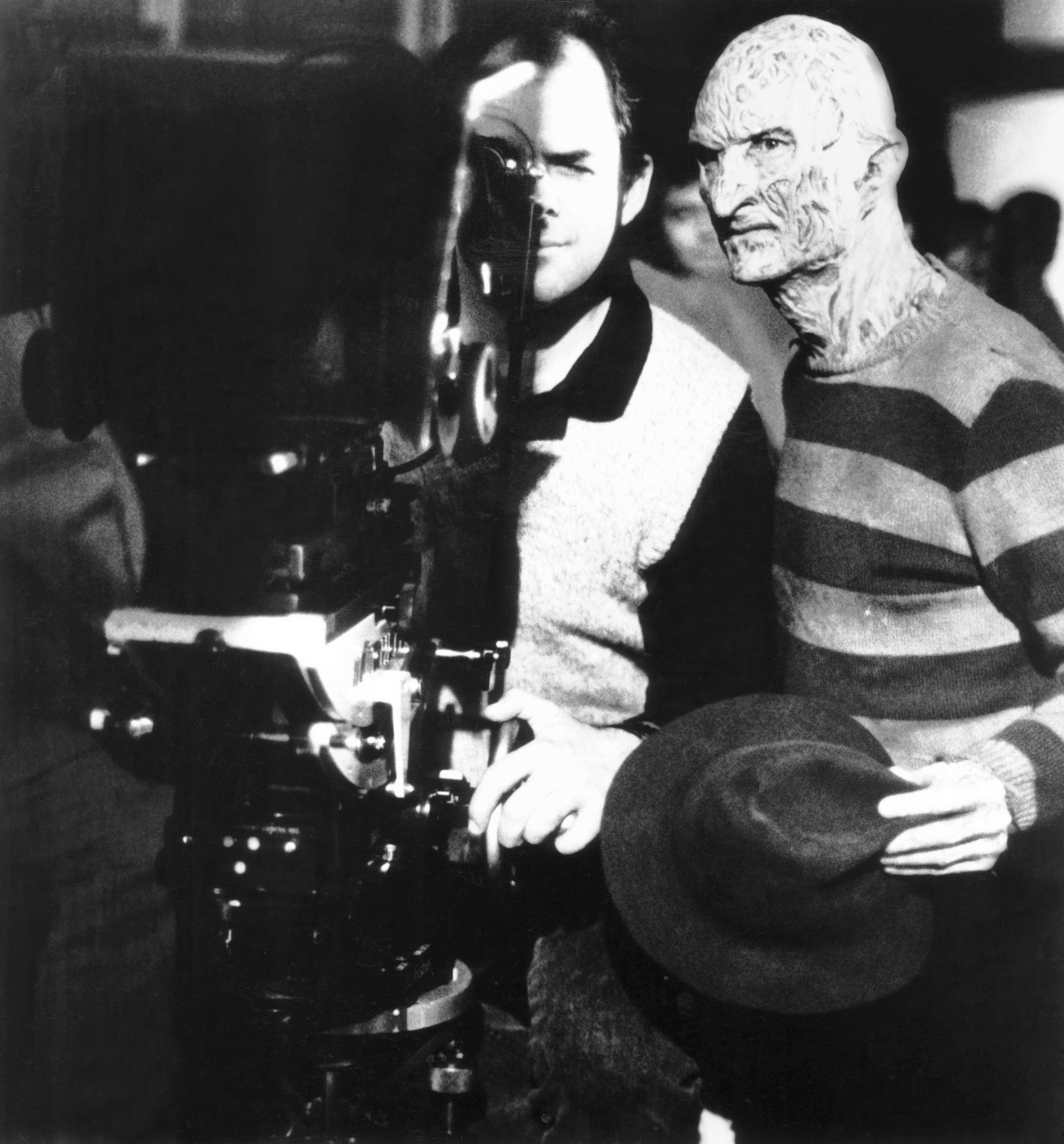 A man in a nightmareish costume stands behind a camera