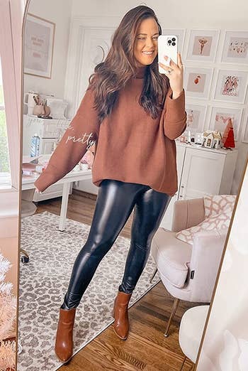 reviewer wearing the brown sweater with black leather leggings and boots