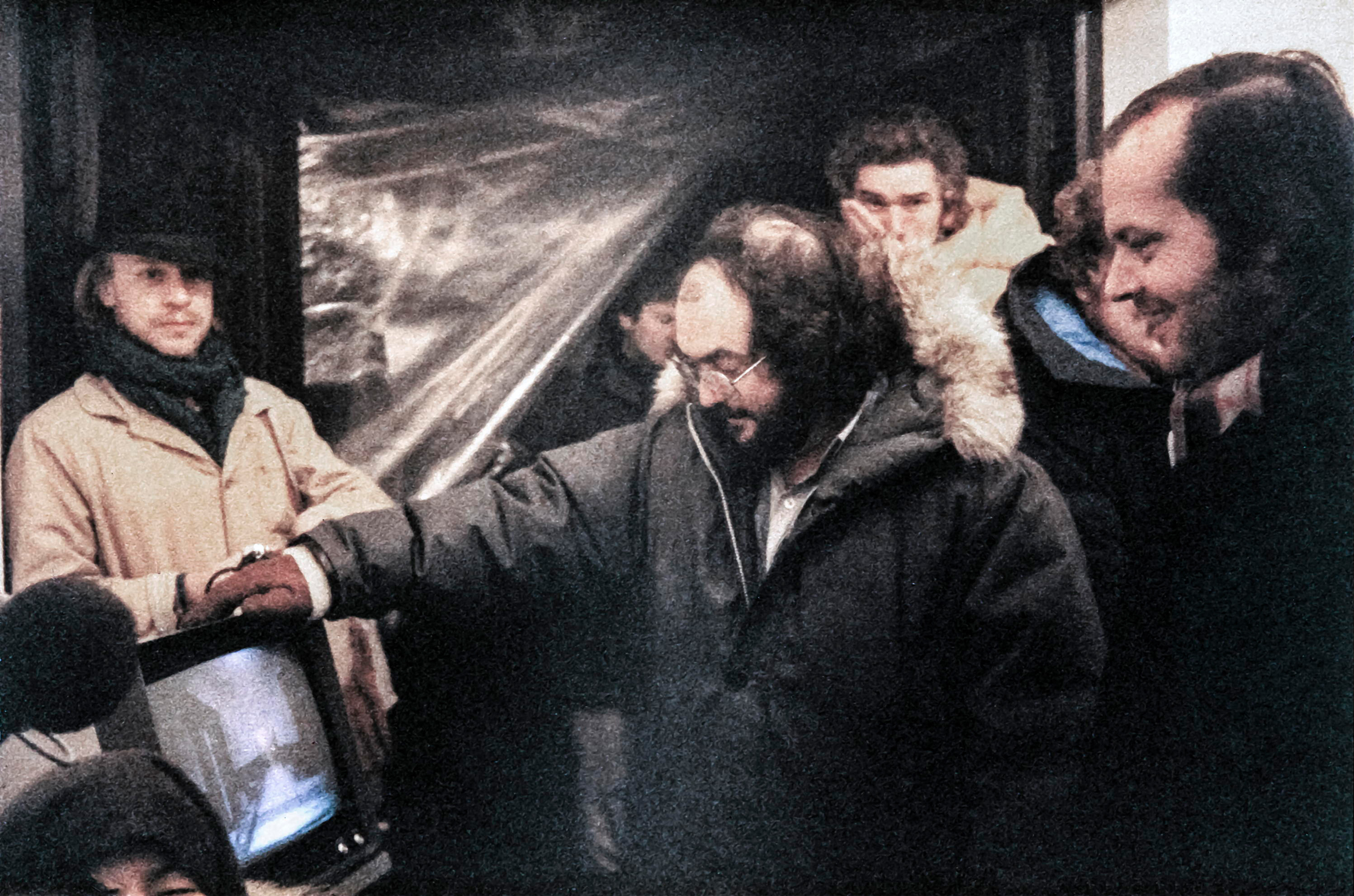 A group of men in winter coats watch a monitor