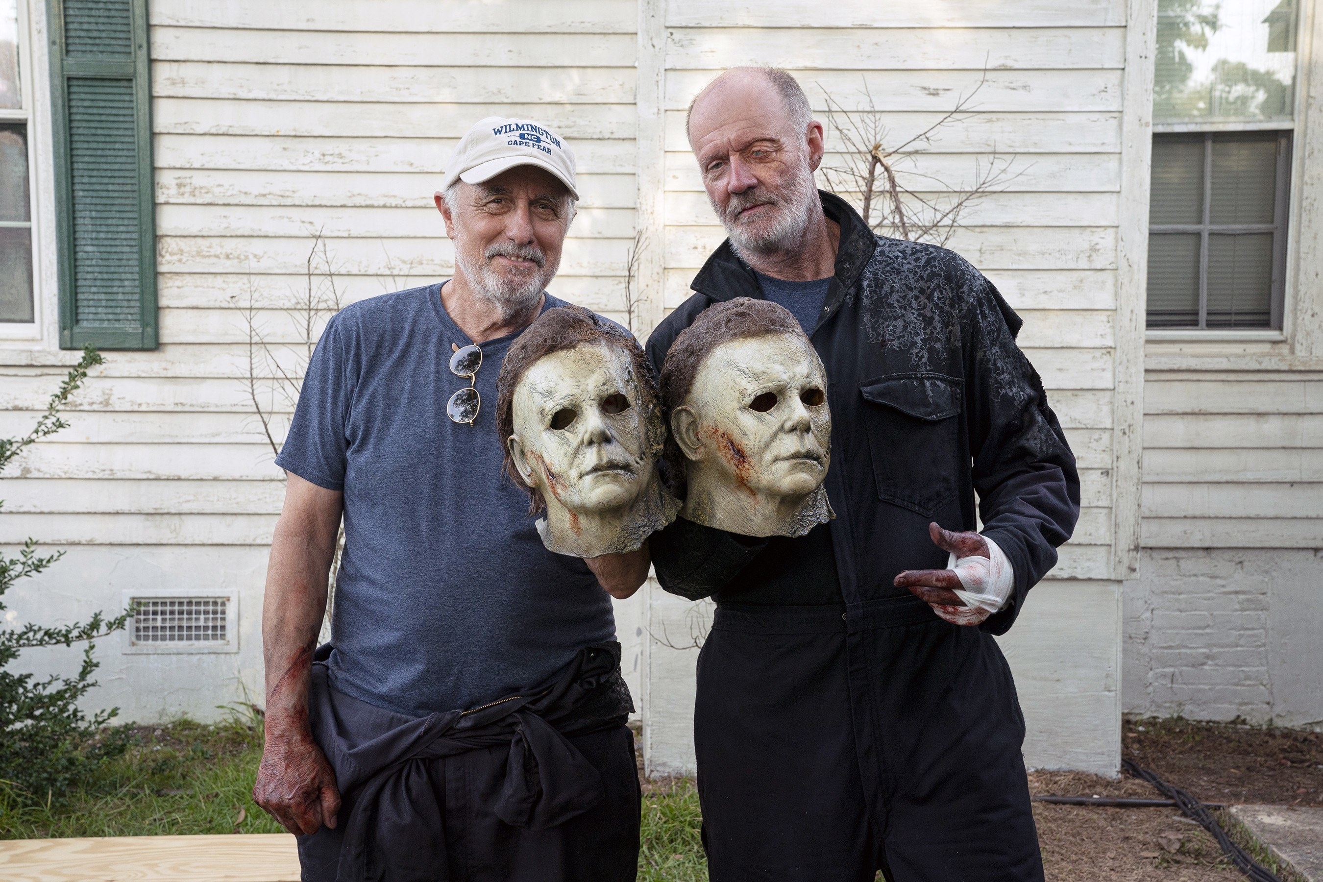 Two men pose holding masks on set