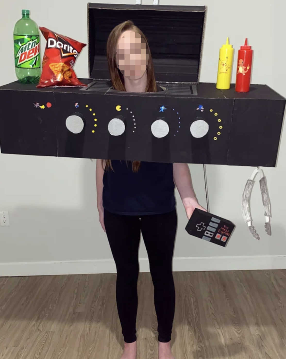 A girl in the middle of a grill costume with snacks and condiments on top, holding a gaming console