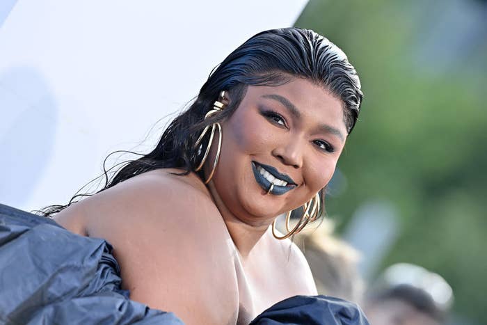 Lizzo smiling on the red carpet and rocking a lip ring and large hoop earrings