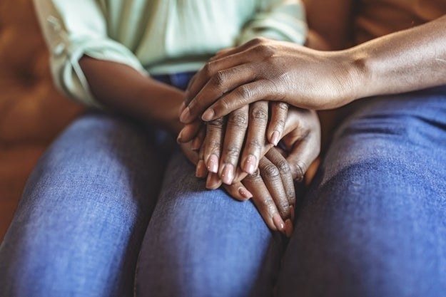 Closeup shot of an unrecognizable couple holding hands while sitting on sofa in the living room at home