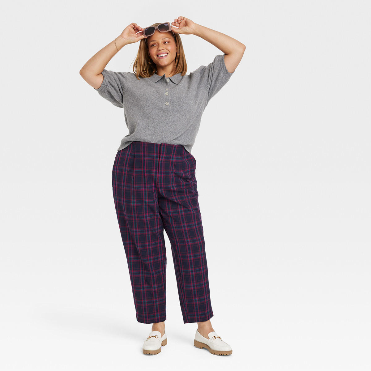Smiling woman hold sunglasses while wearing polo shirt and plaid pants