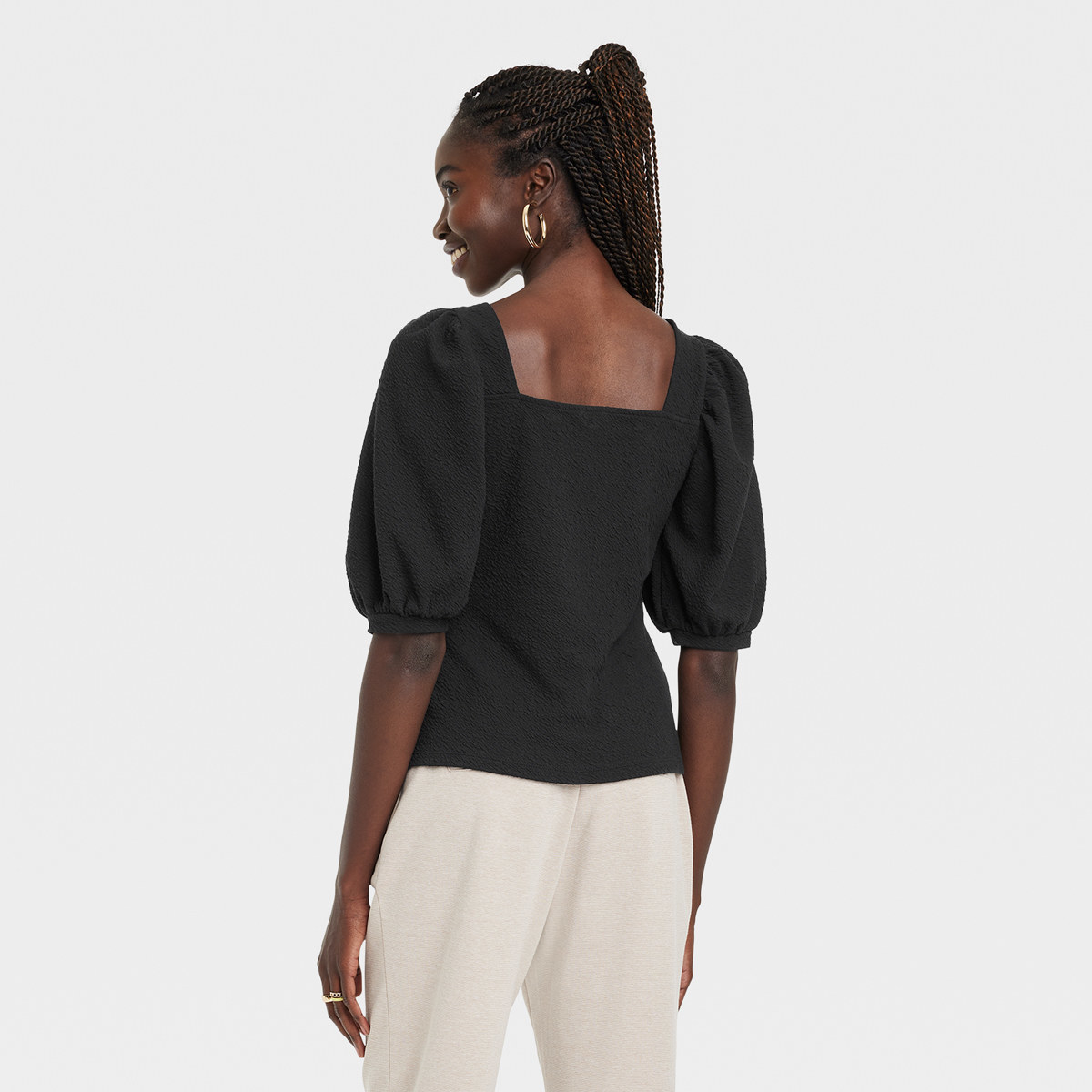 Woman wears square neck shirt with puffy sleeves and gold hoops