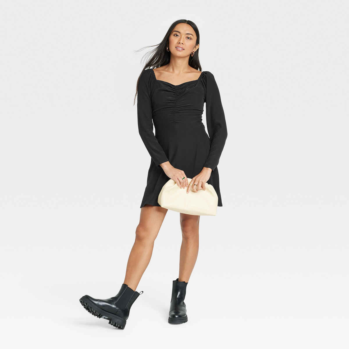 Woman sports flirty look of short black dress, chunky boots and white clutch