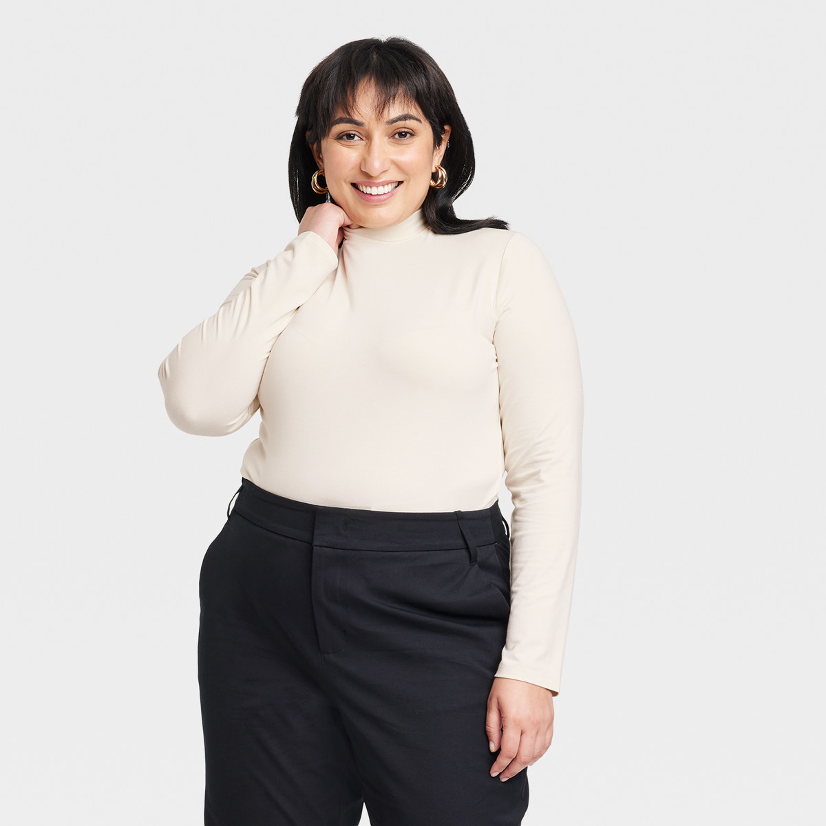 Woman strikes cute pose while wearing turtleneck and formal pants