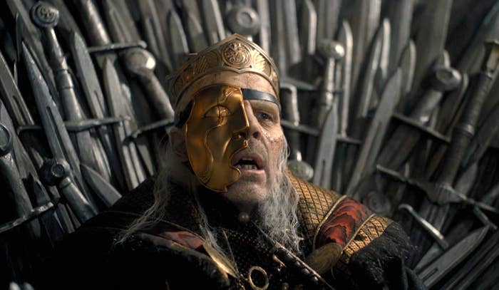 Viserys sitting on the thrown with a half mask made of gold
