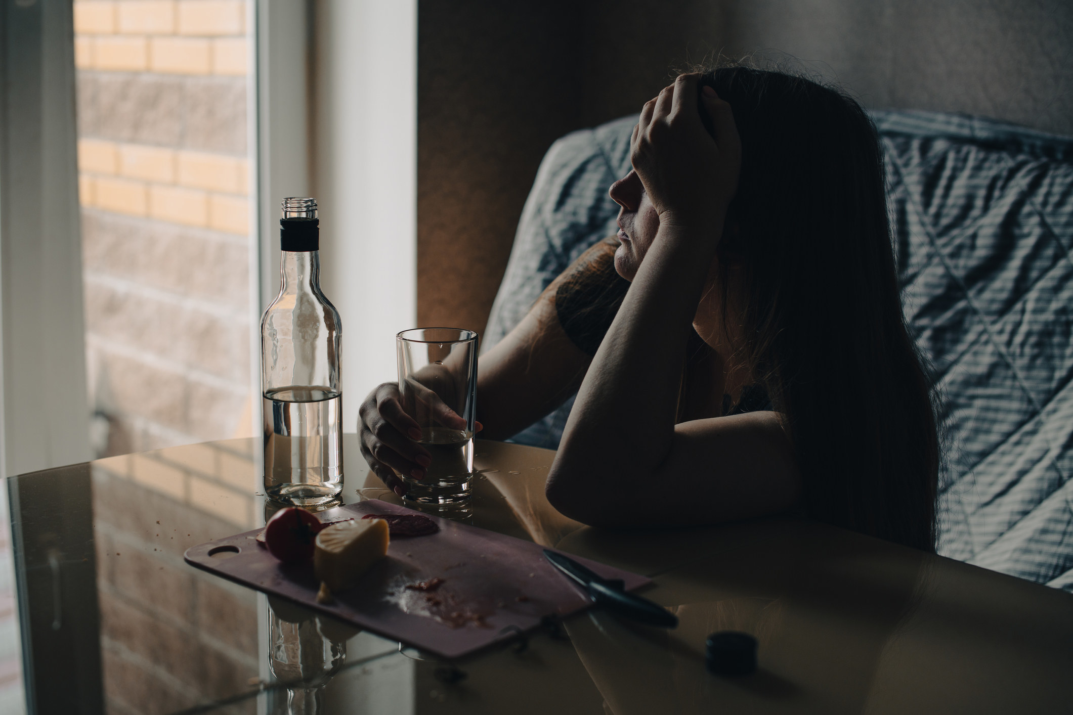 A person sitting at a table holding a glass and looking out a window