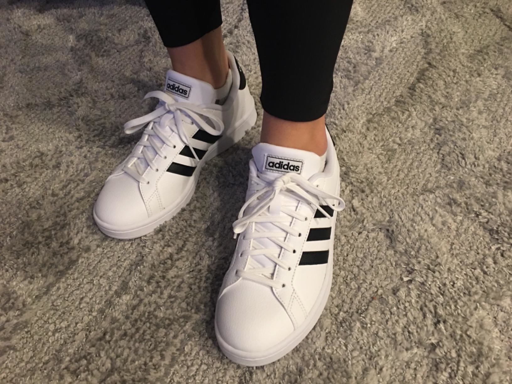 reviewer wearing white adidas shoes with black stripes on the side