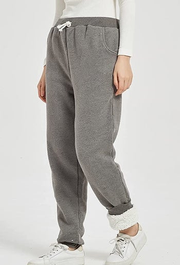 a model wearing gray sweatpants with one ankle rolled up to reveal the fleece-lining, plus white sneakers