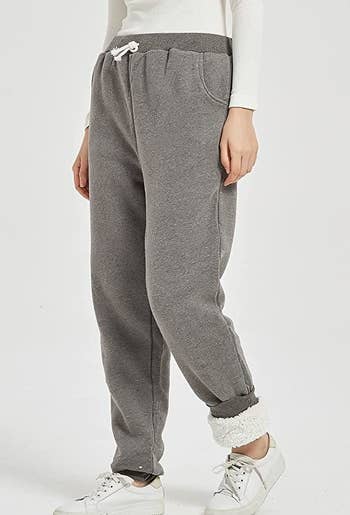 a model wearing gray sweatpants with one ankle rolled up to reveal the fleece-lining, plus white sneakers